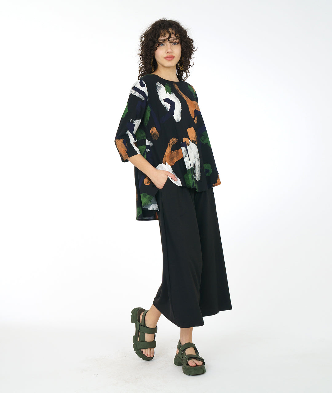 model in a wide leg black pant with a multi color paint stroke print pull over top with a high-low hem, 3/4 sleeves and a full bodied back