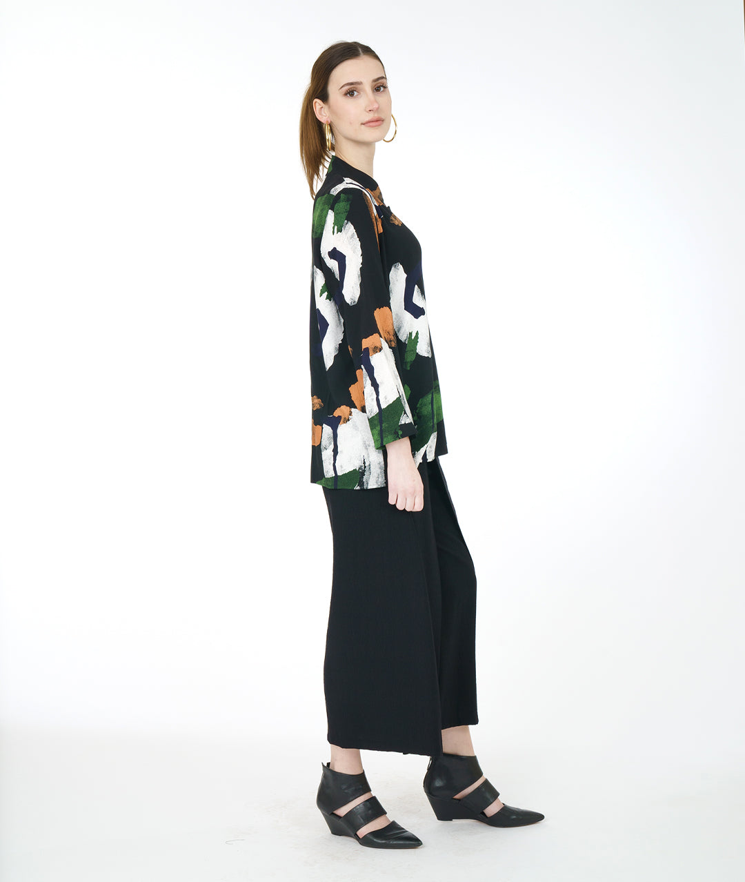 model in a wide leg black pant with a black button down blouse with a green, white and orange paint stroke print