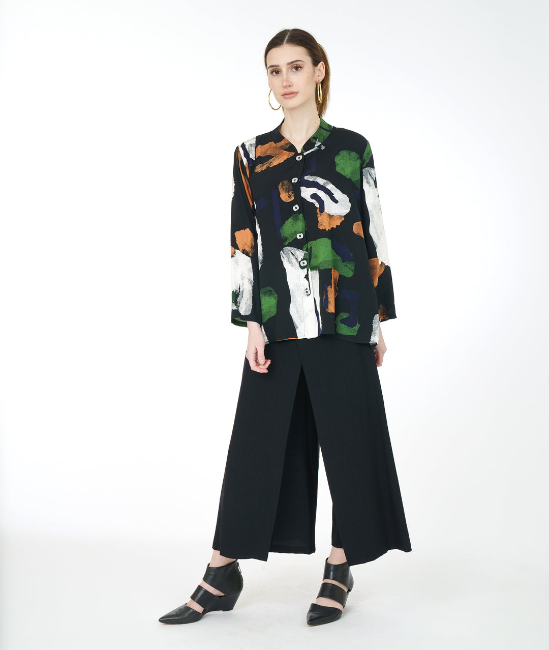 model in a wide leg black pant with a black button down blouse with a green, white and orange paint stroke print