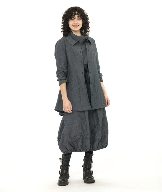 model wearing dark grey button down jacket with long sleeves, a round collar and high-low hem with a bubble skirt, cowl neck top and black boots.