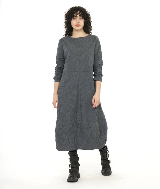 model wearing midi length dress with long sleeves, rounded neckline and lantern shaped skirt with black boots; bodice and skirt have angled seams coming to a point at the center front.