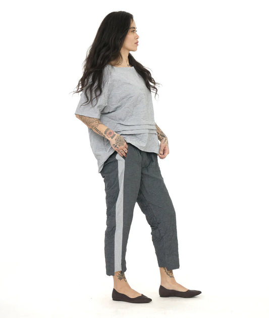 model wearing light grey top pleated in the front with dark grey pants that have a light grey contrasting panel on the side.