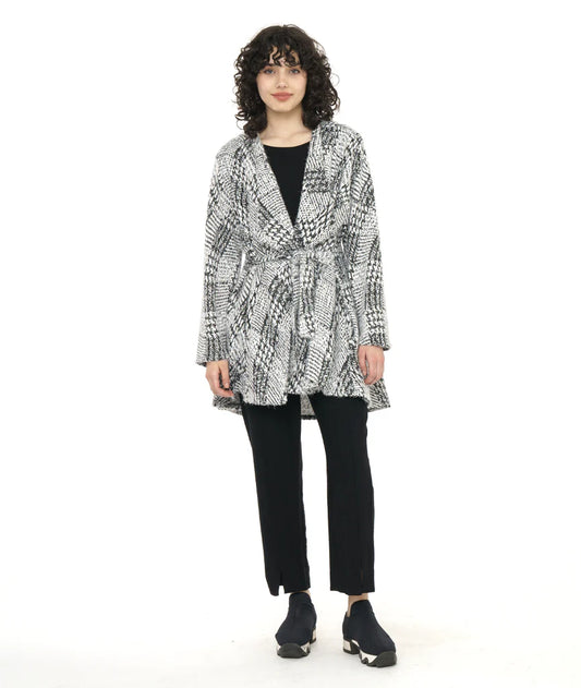 model wearing black and white pattern jacket with matching waist tie and large collar, a black top, black pants and sneakers