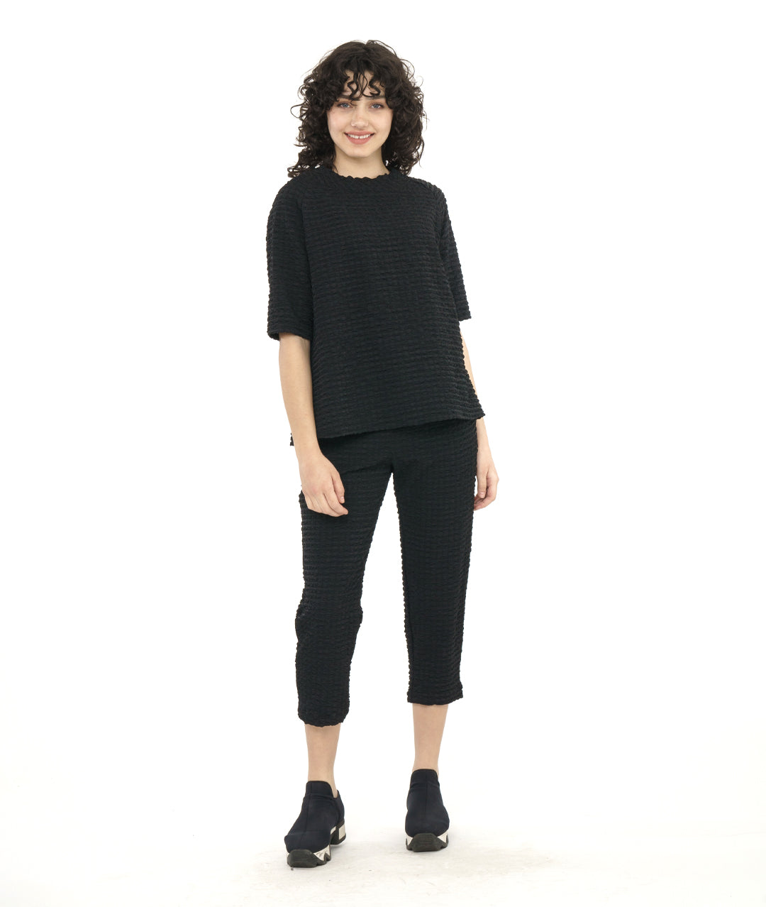 model in a black textured pullover top with a raglan sleeve an portrait collar. worn with a matching black crop pant 
