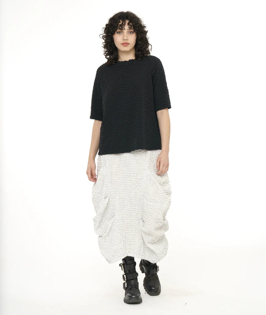 model wearing long white shirt pleated on sides with black top and boots.