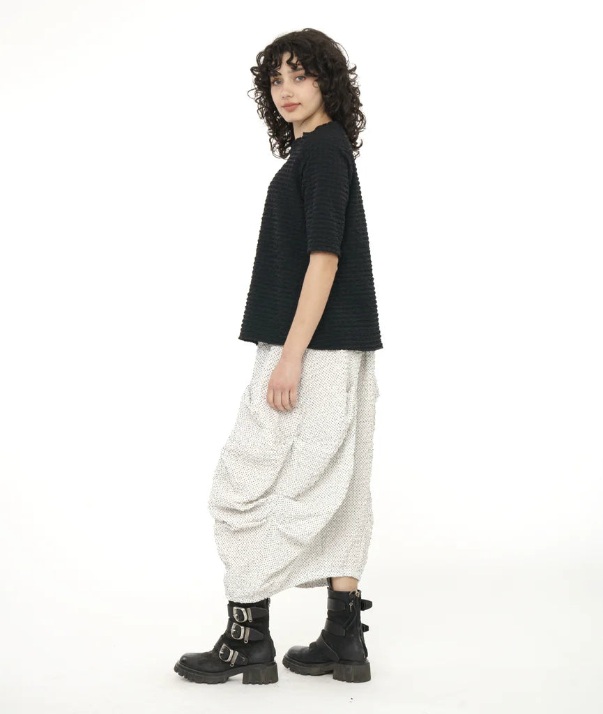 model wearing long white shirt pleated on sides with black top and boots.