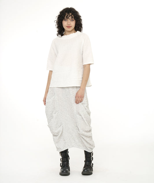 model in a black and white dot print skirt and a white boxy pullover top with short raglan sleeves, a standing collar and a straight hem