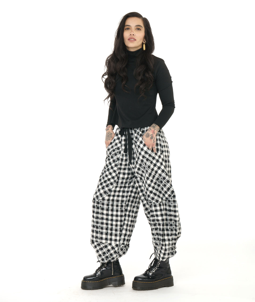 model in a black tee and a black and white grid print pants with deep exterior pockets, a wide leg tapering at the ankle, and a black twill tie belt