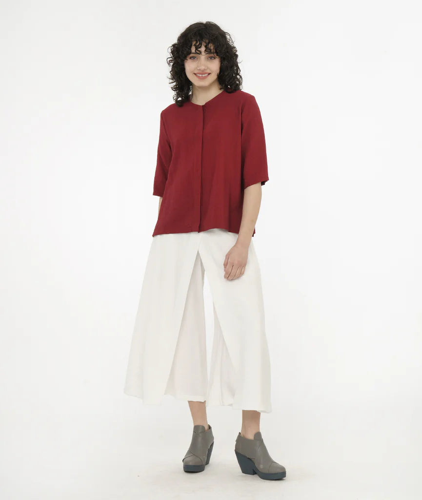 model wearing brick red top with a hidden buttoned placket, 3/4 sleeves, and a round neckline worn with white pants.