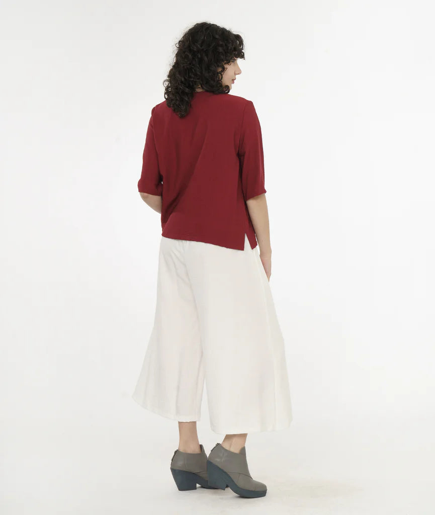 model wearing brick red top with a hidden buttoned placket, 3/4 sleeves, and a round neckline worn with white pants.