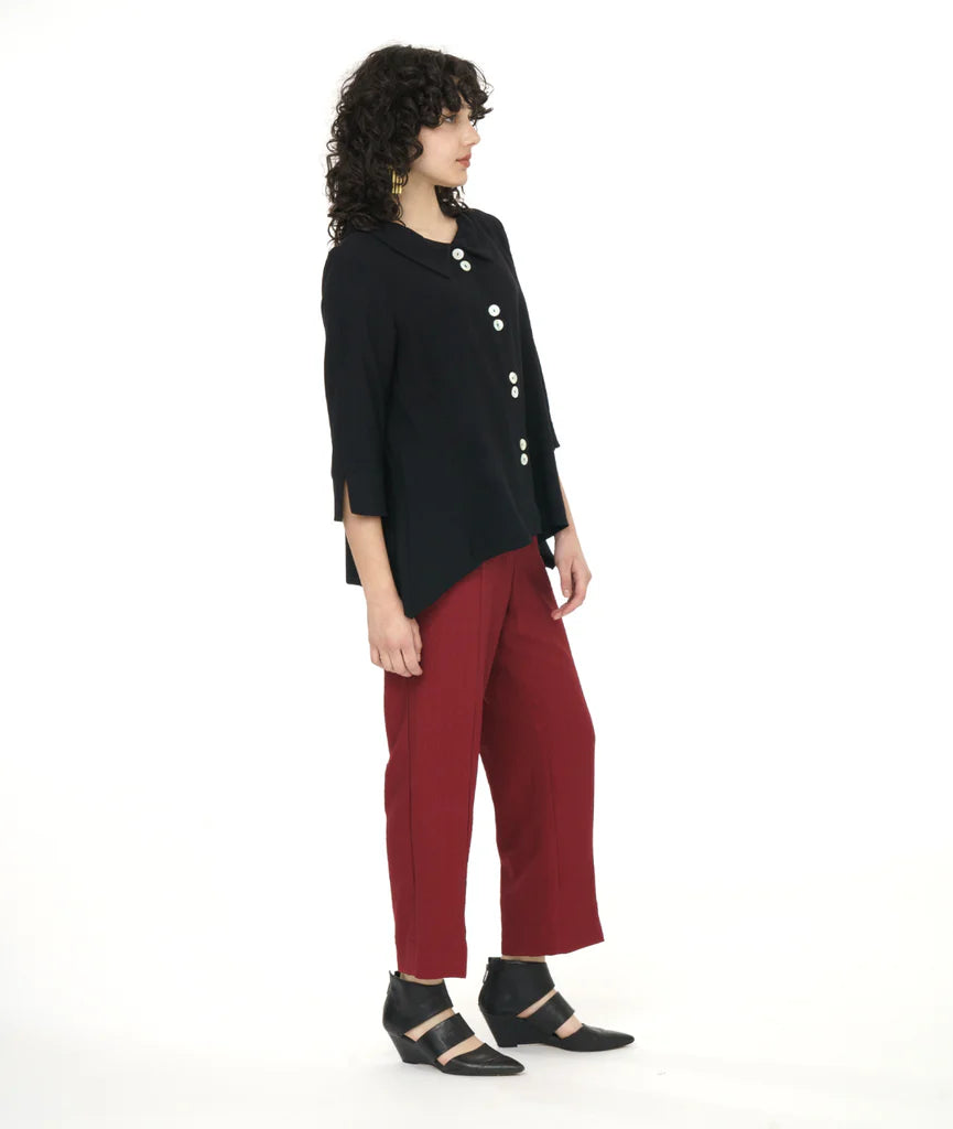 model in a straight leg red pant worn with a black button down bouse with four sets of double buttons, a rounded collar, 3/4 sleeves and deep dips in the side hem