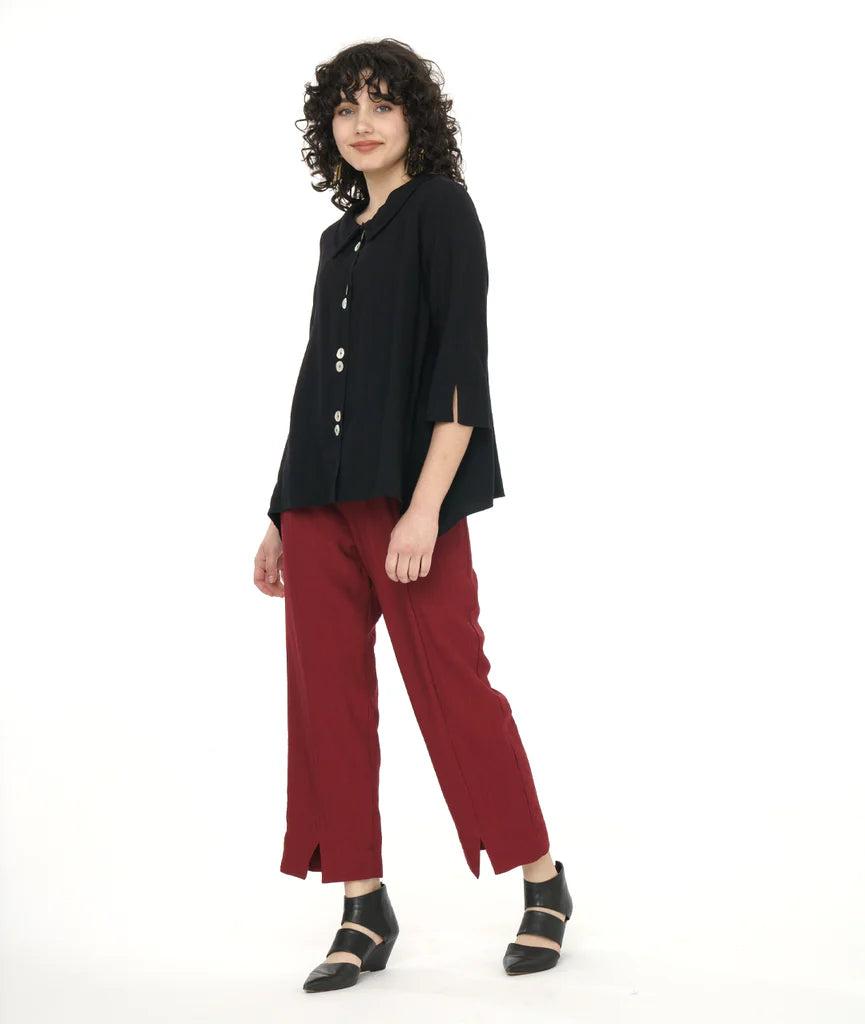 model in a straight leg red pant worn with a black button down bouse with four sets of double buttons, a rounded collar, 3/4 sleeves and deep dips in the side hem