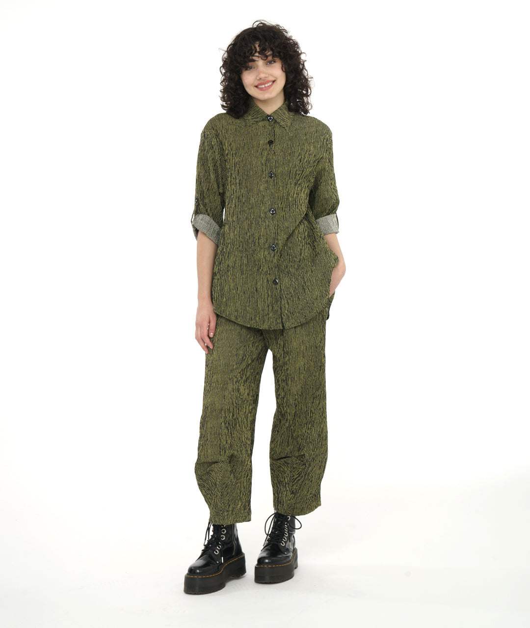 model in a green and black stripe blouse with rolled sleeves, worn with a matching pant with a tulip shape made from pleating below the knee