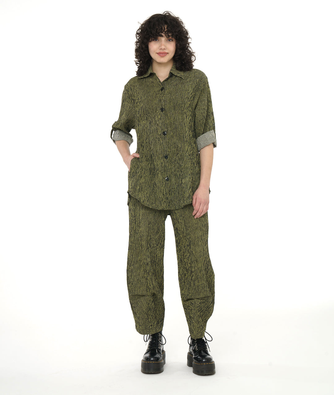 model in a black and olive green elastic waist pull on pant with pockets. Tulip shape with pinch pleats below the knee, worn with a matching button down blouse