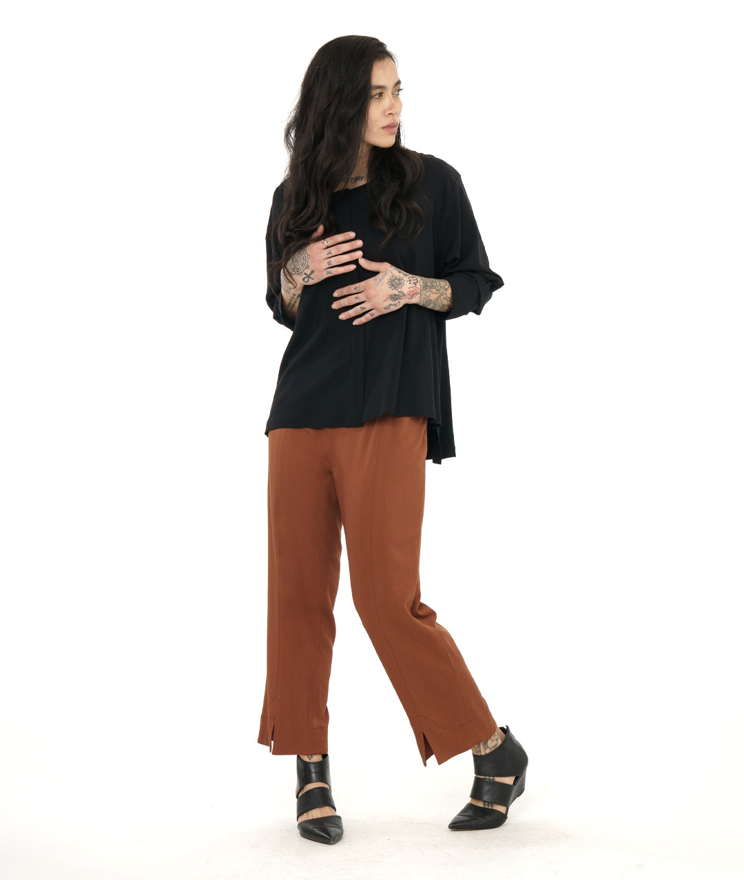 model in a rust color straight cut pant, worn with a black pullover top with long sleeves and a stair step hem