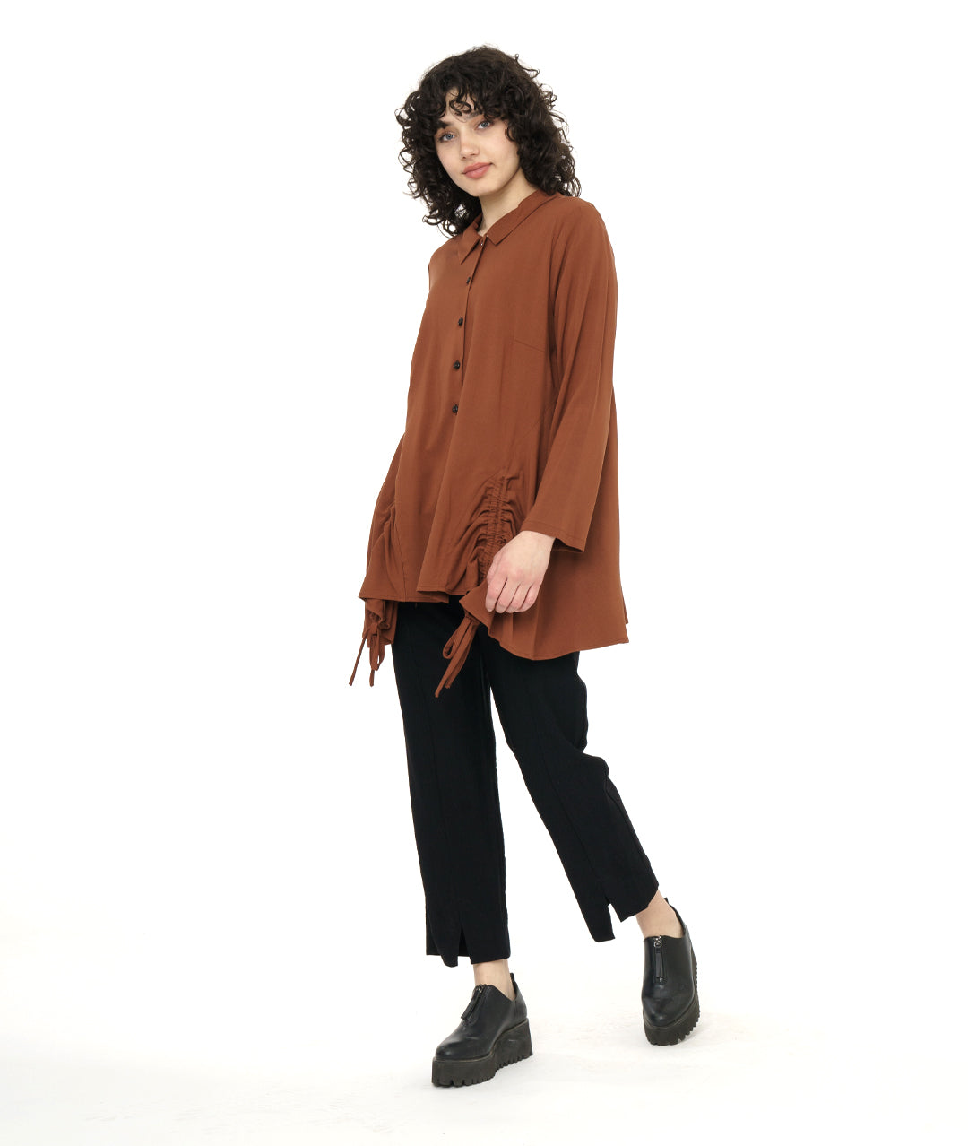 model in a straight leg black pant with a rust color button down blouse with a gathered detail at each front hip