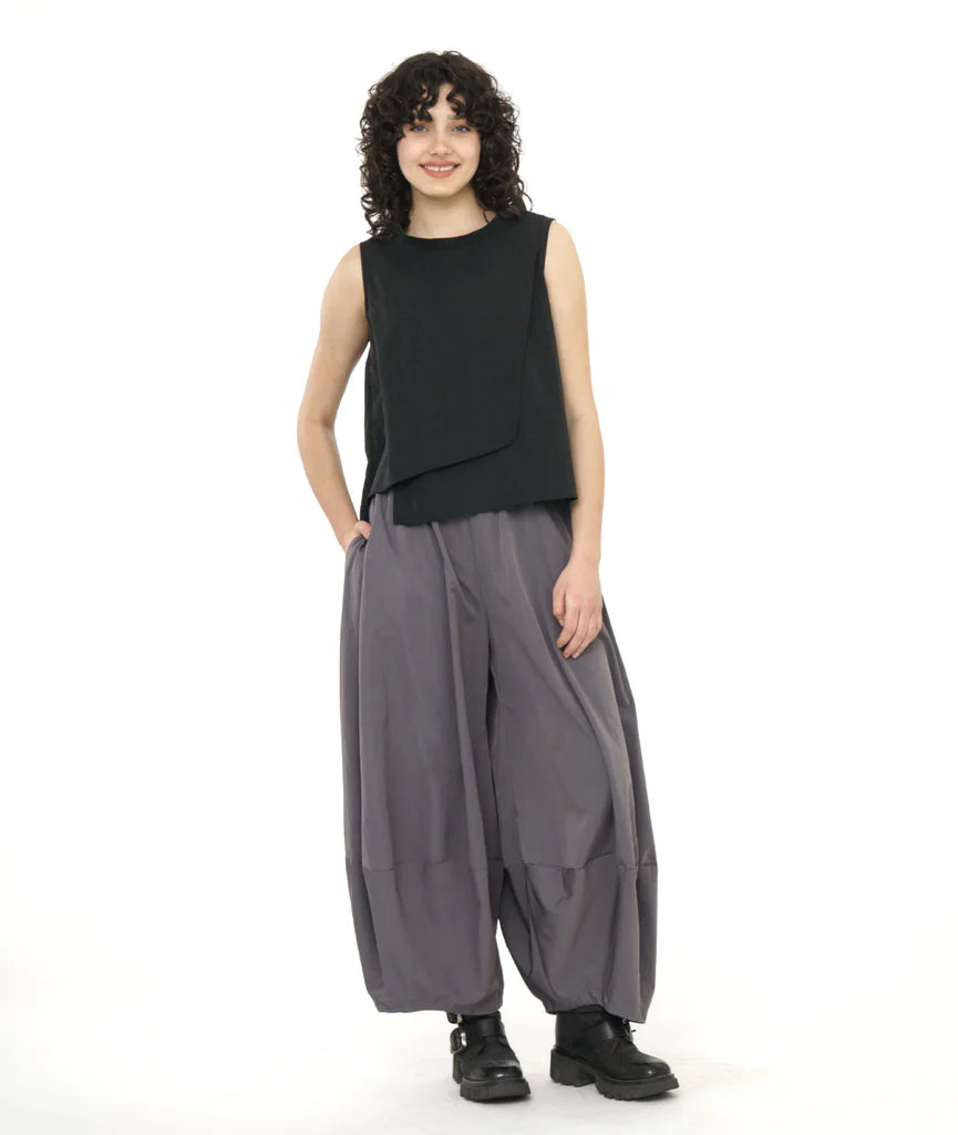 model in a black asymmetrical sleevelss top, worn with a wide leg grey pant with an elastic waist and a taperd ankle, creating a tulip shaped silhouette