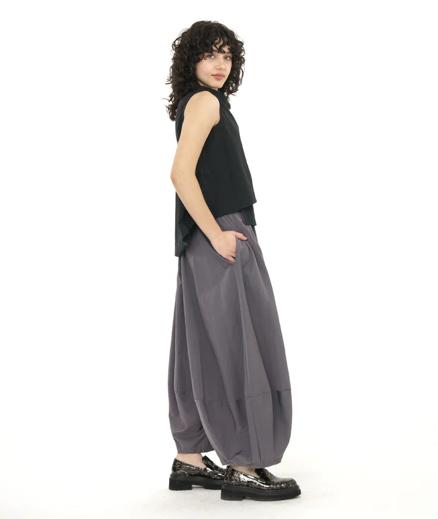 model in a black asymmetrical sleevelss top, worn with a wide leg grey pant with an elastic waist and a taperd ankle, creating a tulip shaped silhouette