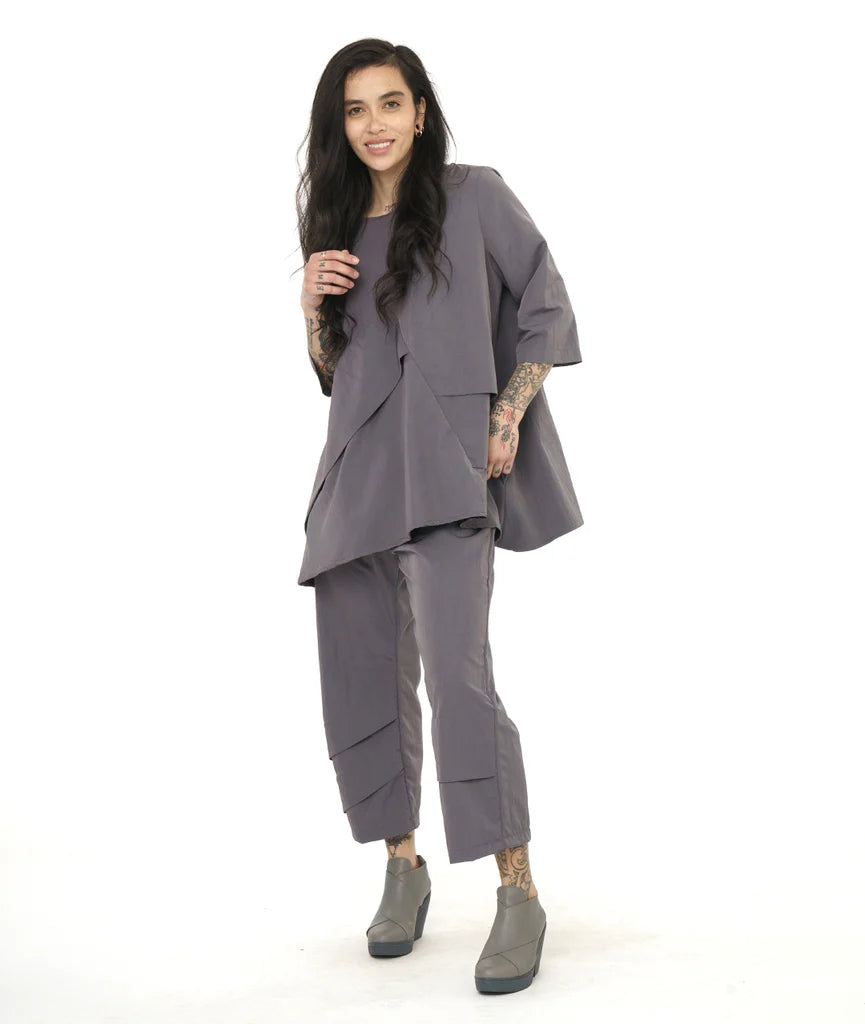 model wearing a grey pullover top with an asymmetrical tuck and seam detail across the body. top has 3/4 sleeves. worn with matching pants with the same tuck detailing along the lower pants legs