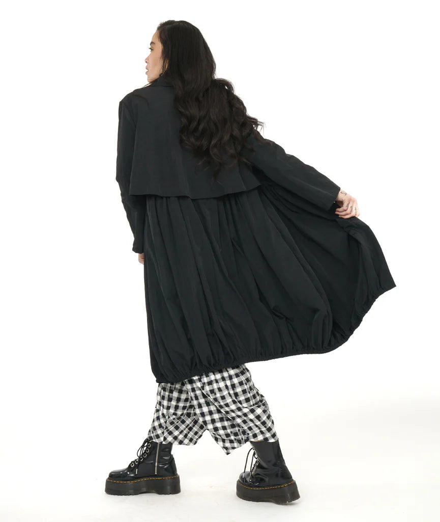 model showing back of black lantern shape long jacket with plaid pants and boots.