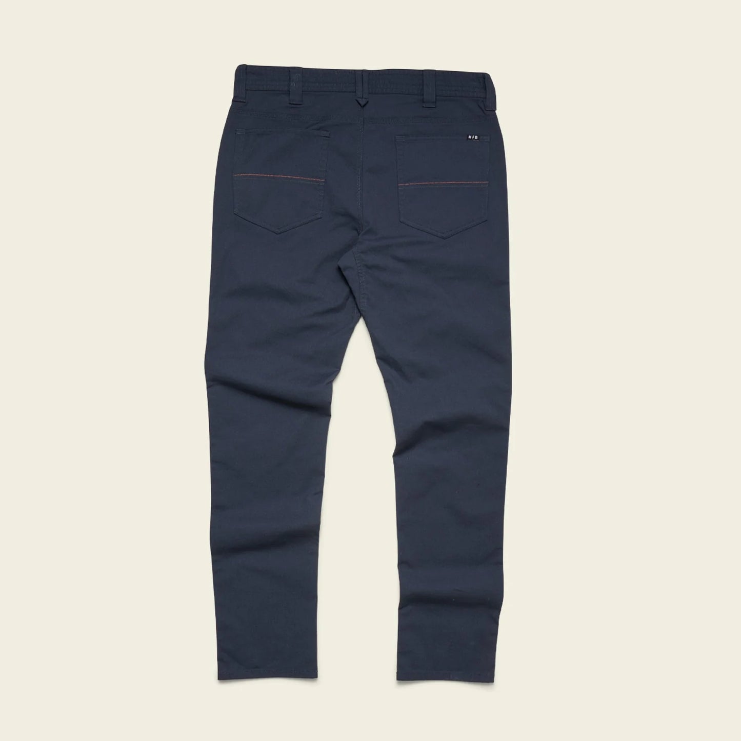 A pair of navy blue slim-fit trousers shown from the back, featuring two back pockets with thin red contrast stitching and a small white embroidered logo on the upper right pocket, laid flat against a light beige background.