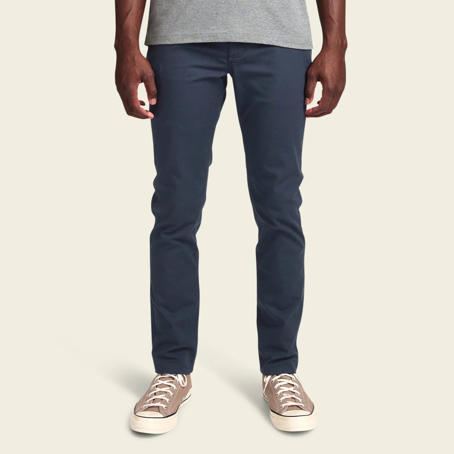 Person wearing navy pants and beige sneakers on a plain background