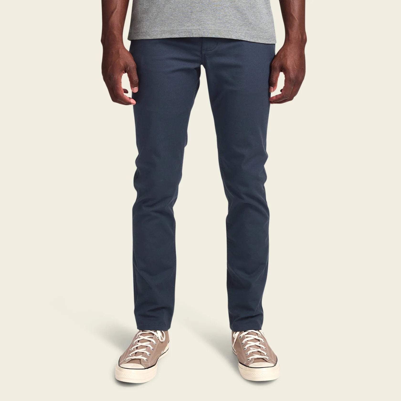 Person wearing navy pants and beige sneakers on a plain background