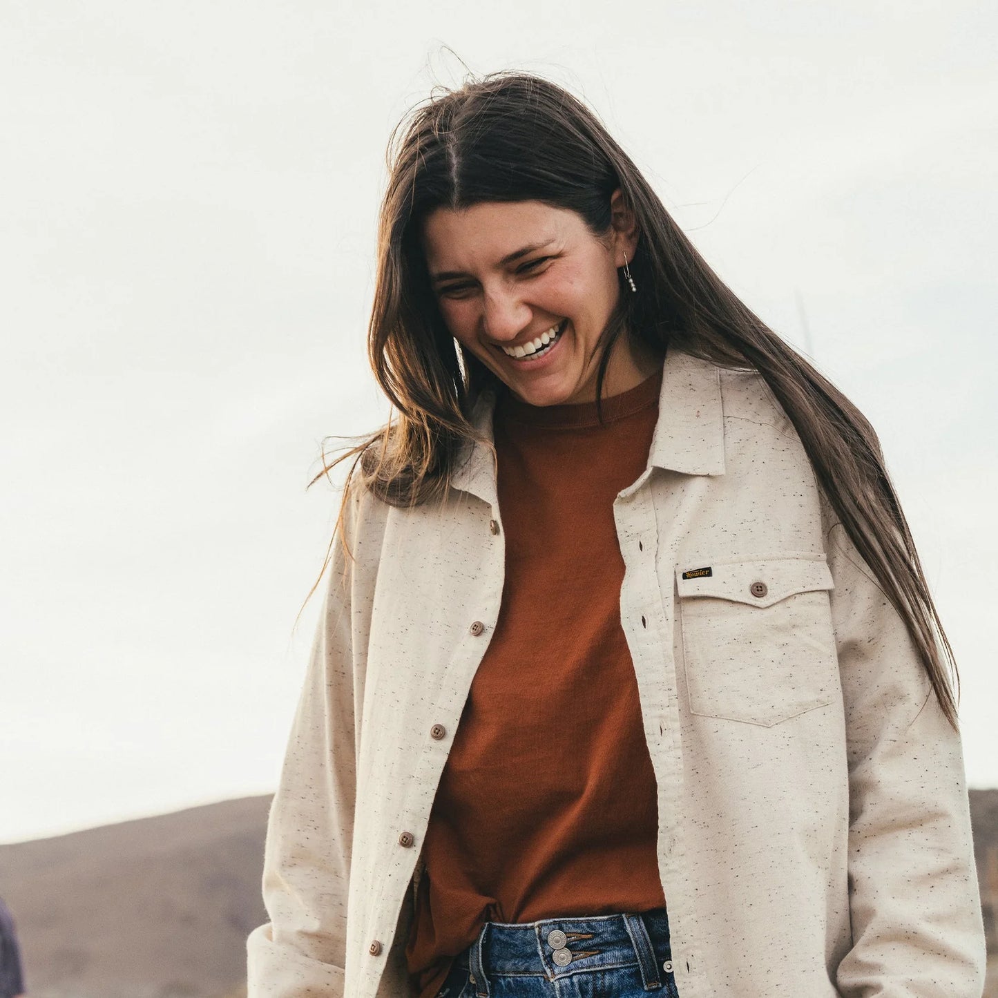Woman wearing a beige flannel over a brown shirt with a blurred background