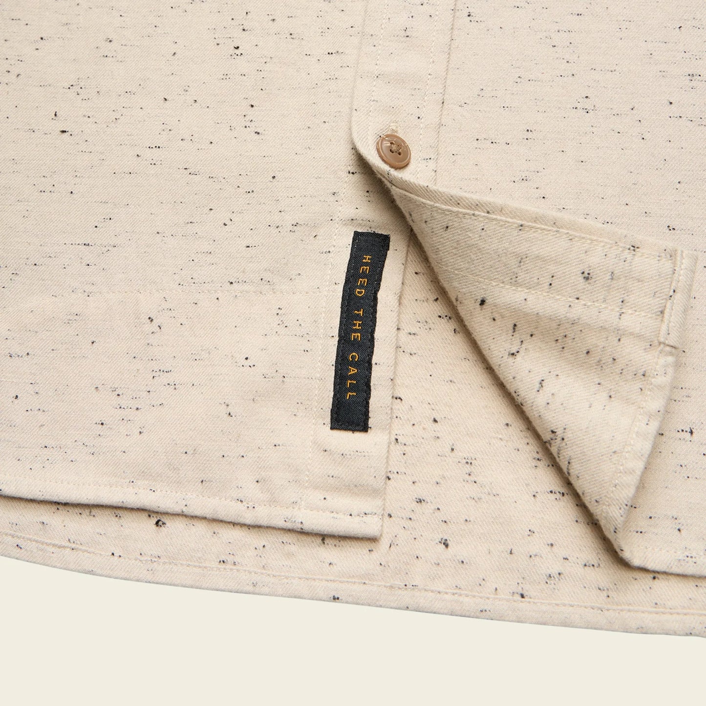 Close-up of a beige textured fabric with a button and a visible brand tag.