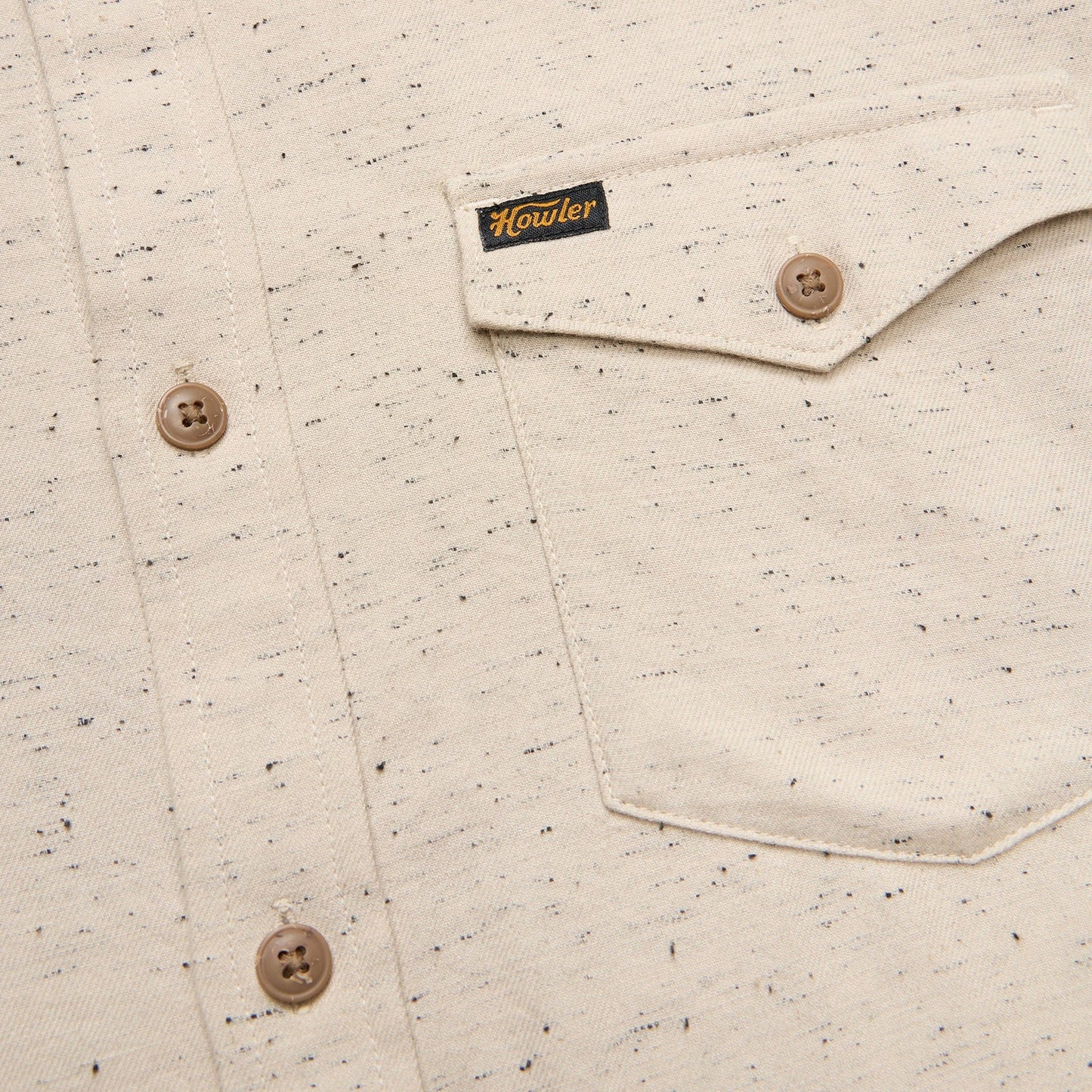 Close-up of a speckled shirt with buttons and a brand label on a beige background