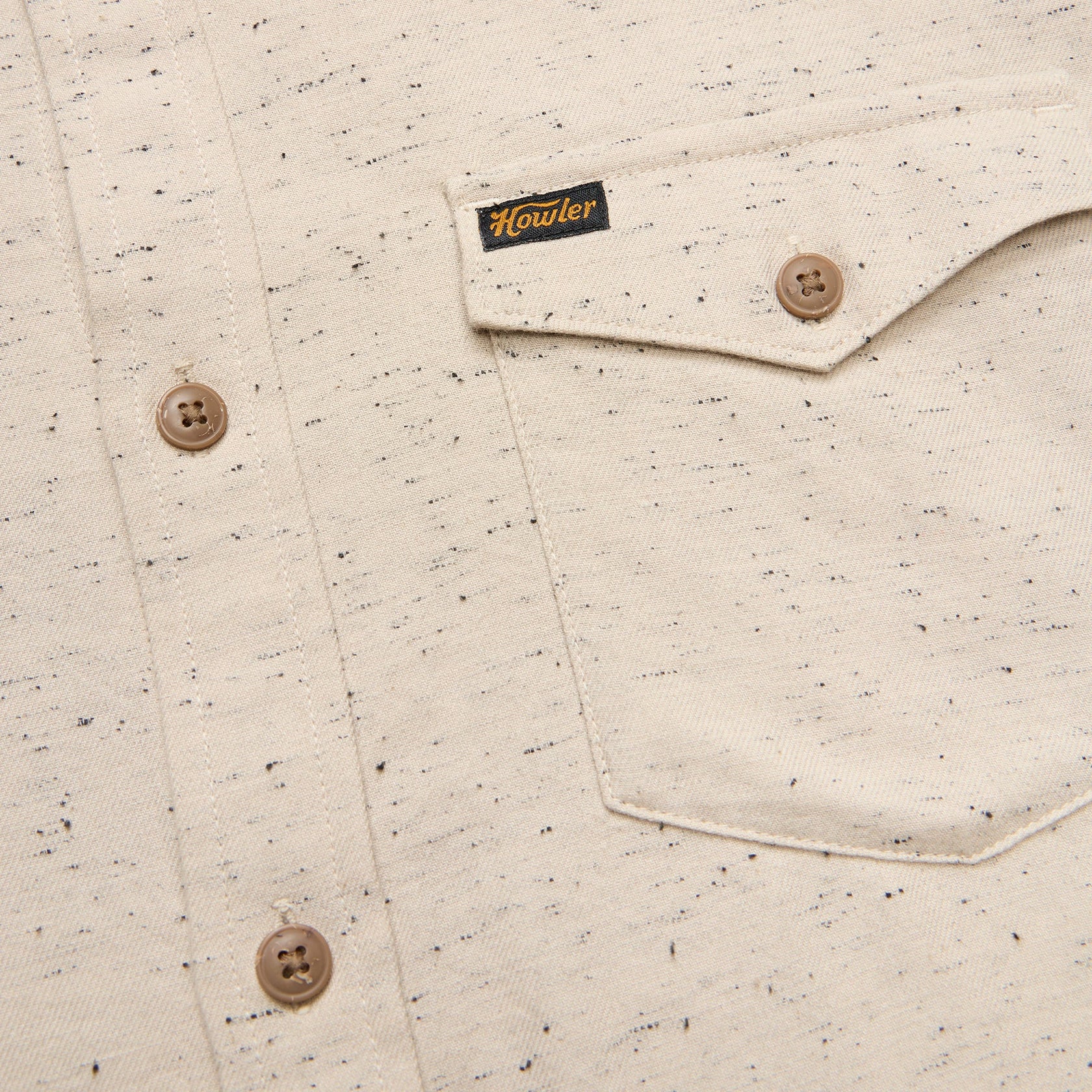 Close-up of a speckled shirt with buttons and a brand label on a beige background