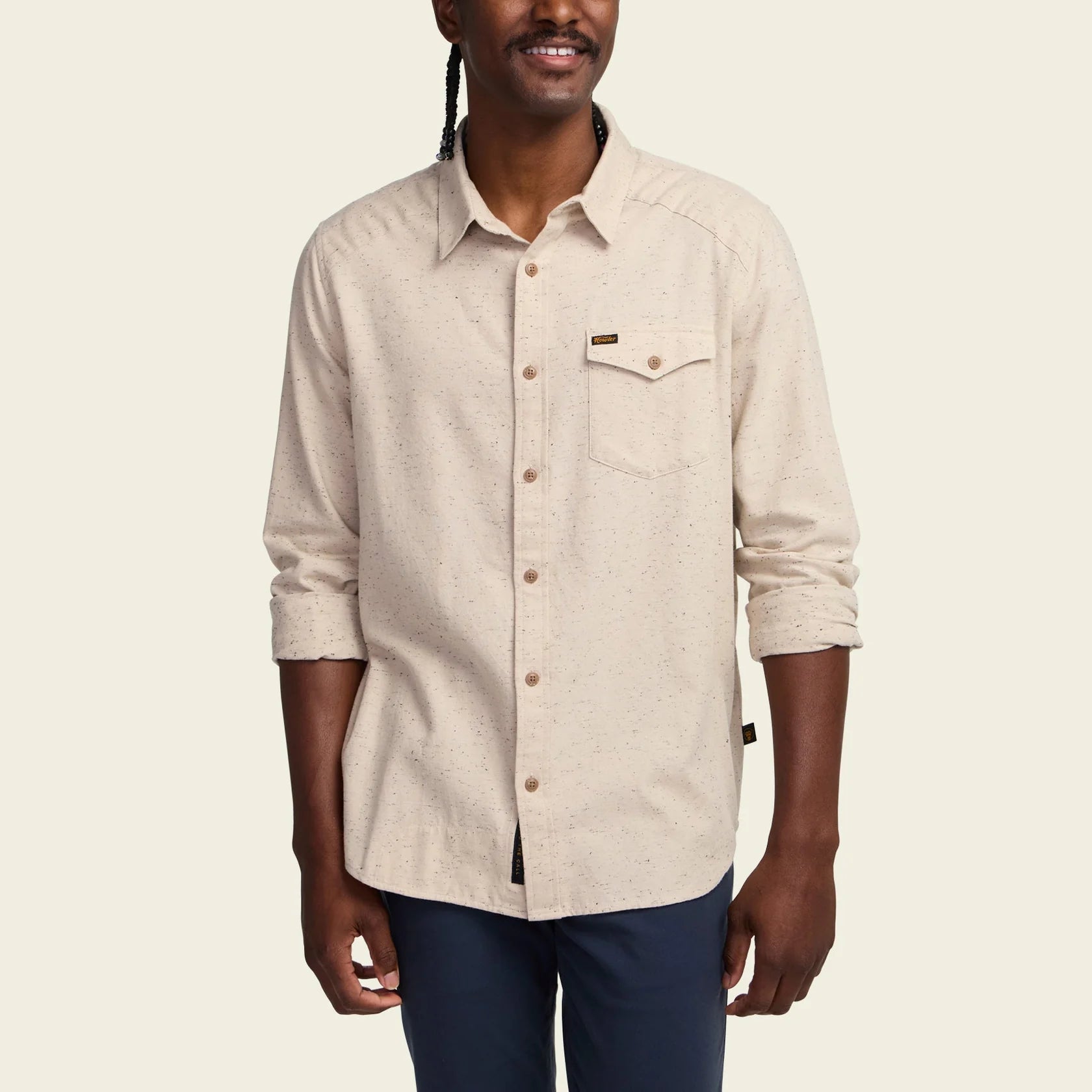 A man wearing a light beige long-sleeve button-up shirt with a chest pocket, shown from the waist up against a plain light background.