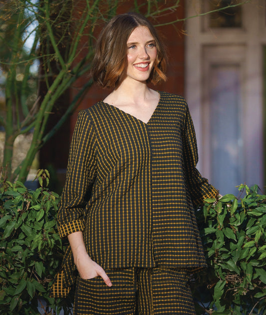 model in a black and yellow check print pullover top with contrasting panels and a v-neck. worn with a matching wide leg pant with an oversized pocket and tapered ankle