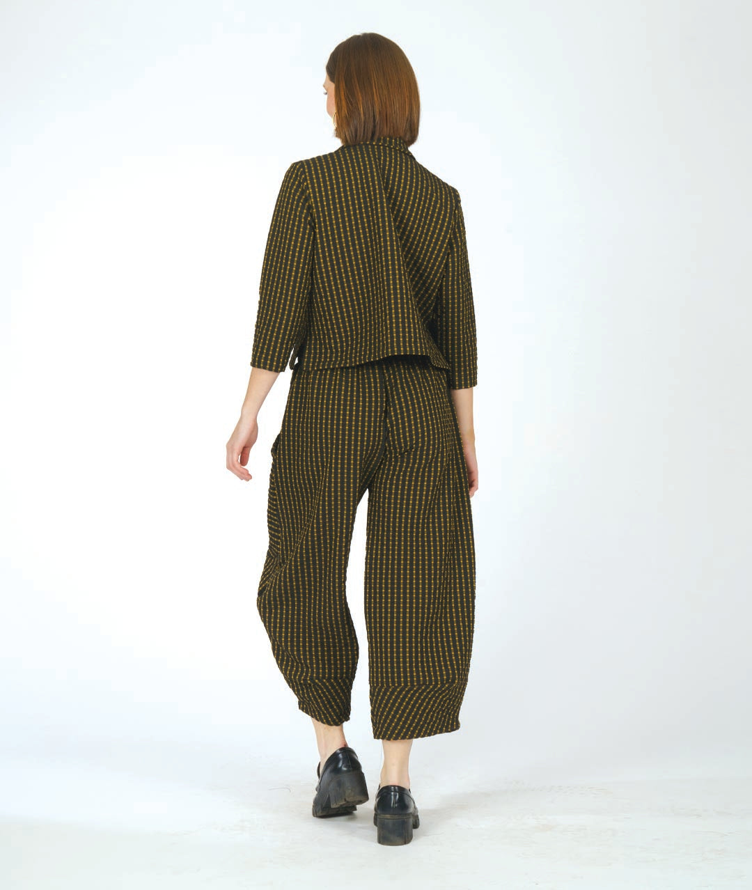 A woman modeling a matching two-piece set consisting of a cropped button-front collared shirt and wide-leg cropped pants, both in a small-scale black and yellow check pattern. She is wearing black loafers with gold hardware against a plain white studio background.