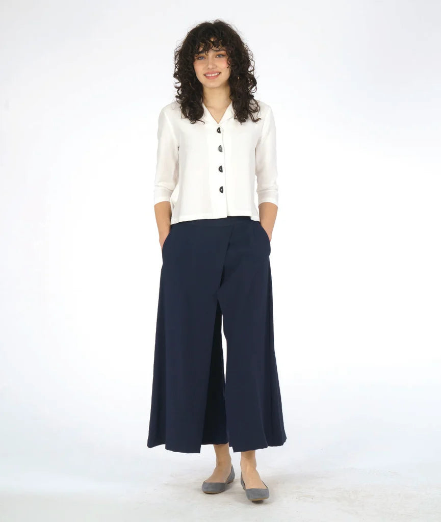 model wearing white button up 3/4 sleeve top with half circle buttons, paired with navy pants and grey shoes