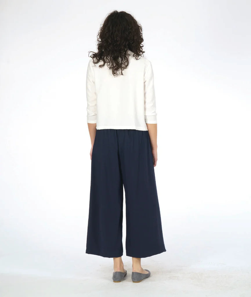 model showing back of white 3/4 sleeve top, paired with navy pants and grey shoes