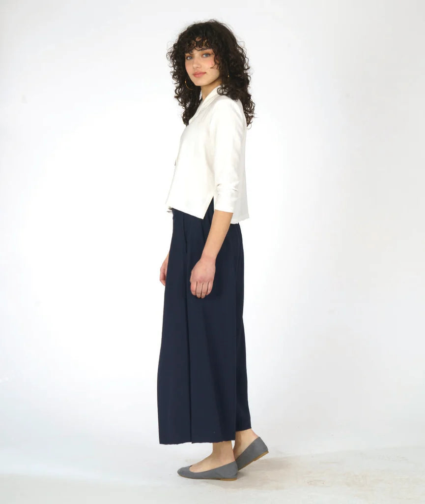 model wearing white button up 3/4 sleeve top with half circle buttons, paired with navy pants and grey shoes