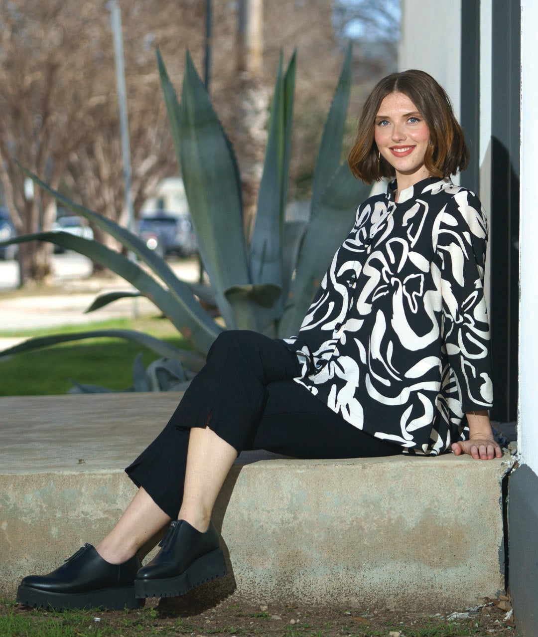 model in a straight cut black pant with a black and ivory floral print blouse with 3/4 sleeves, a mandarin style collar, and black and white buttons down the center front.