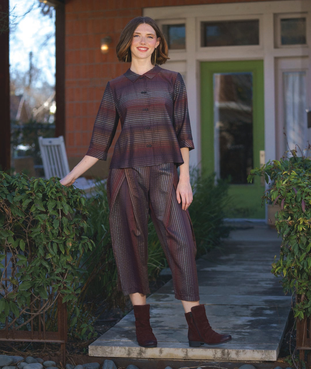model in a boxy button down blouse in a brown and red tone stripe. worn with a matching wide leg pant that overlaps at each hip
