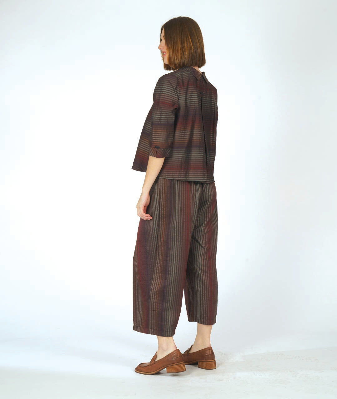 model in a boxy button down blouse in a brown and red tone stripe. worn with a matching wide leg pant that overlaps at each hip