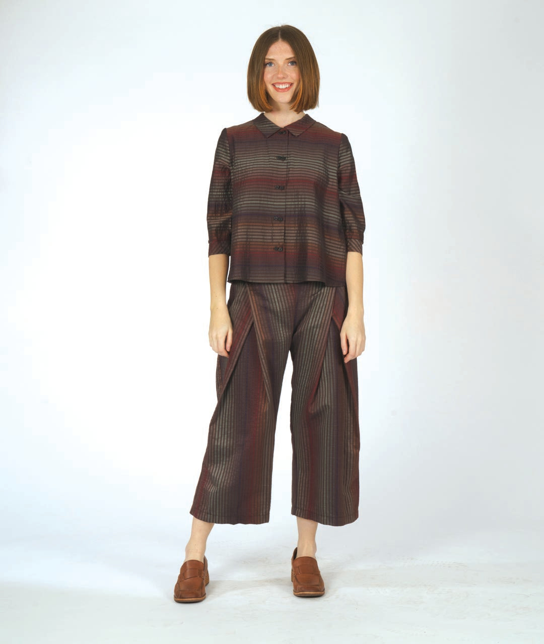 model in a boxy button down blouse in a brown and red tone stripe. worn with a matching wide leg pant that overlaps at each hip