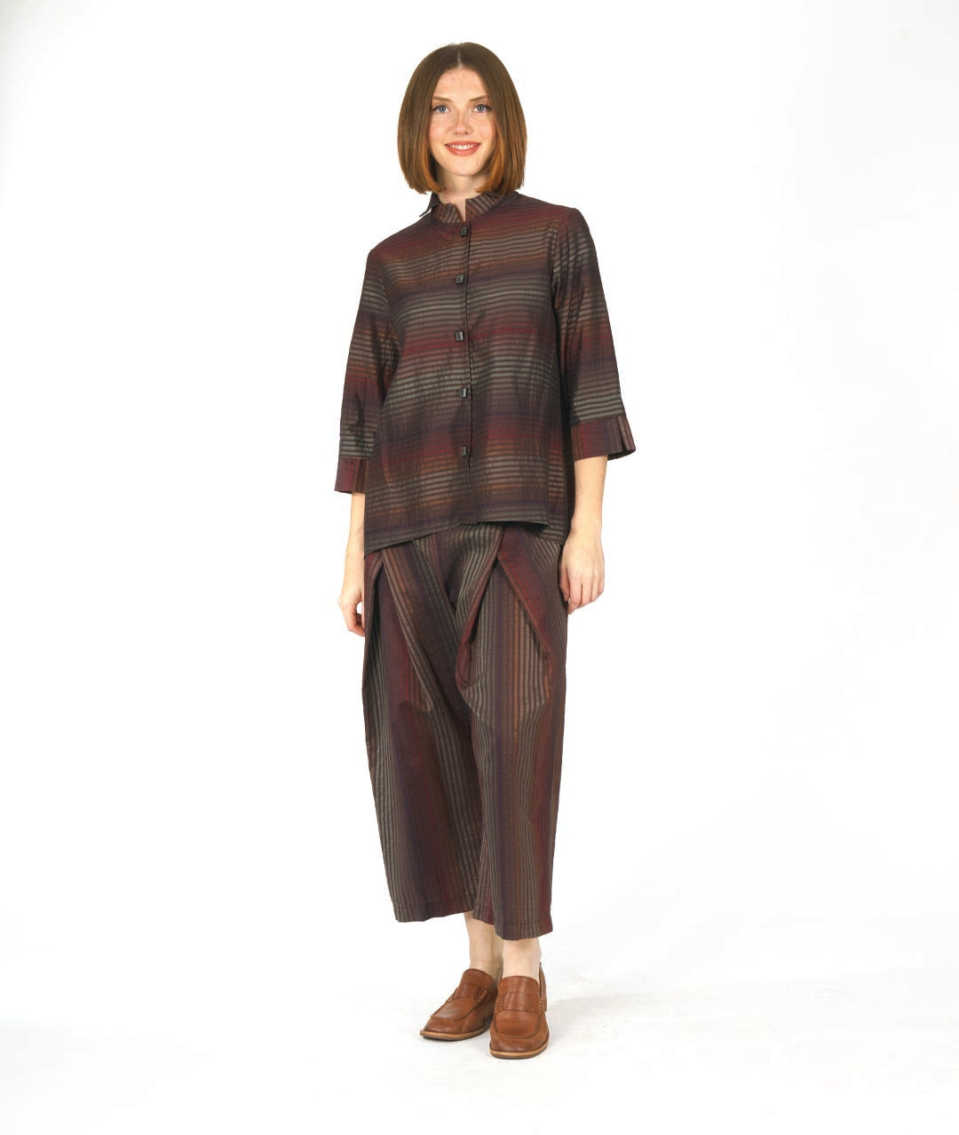 model in a red and brown tone striped pant with an overlap at each thigh. worn with a matching blouse with 3/4 sleeves with a wide cuff and a mandarin style collar