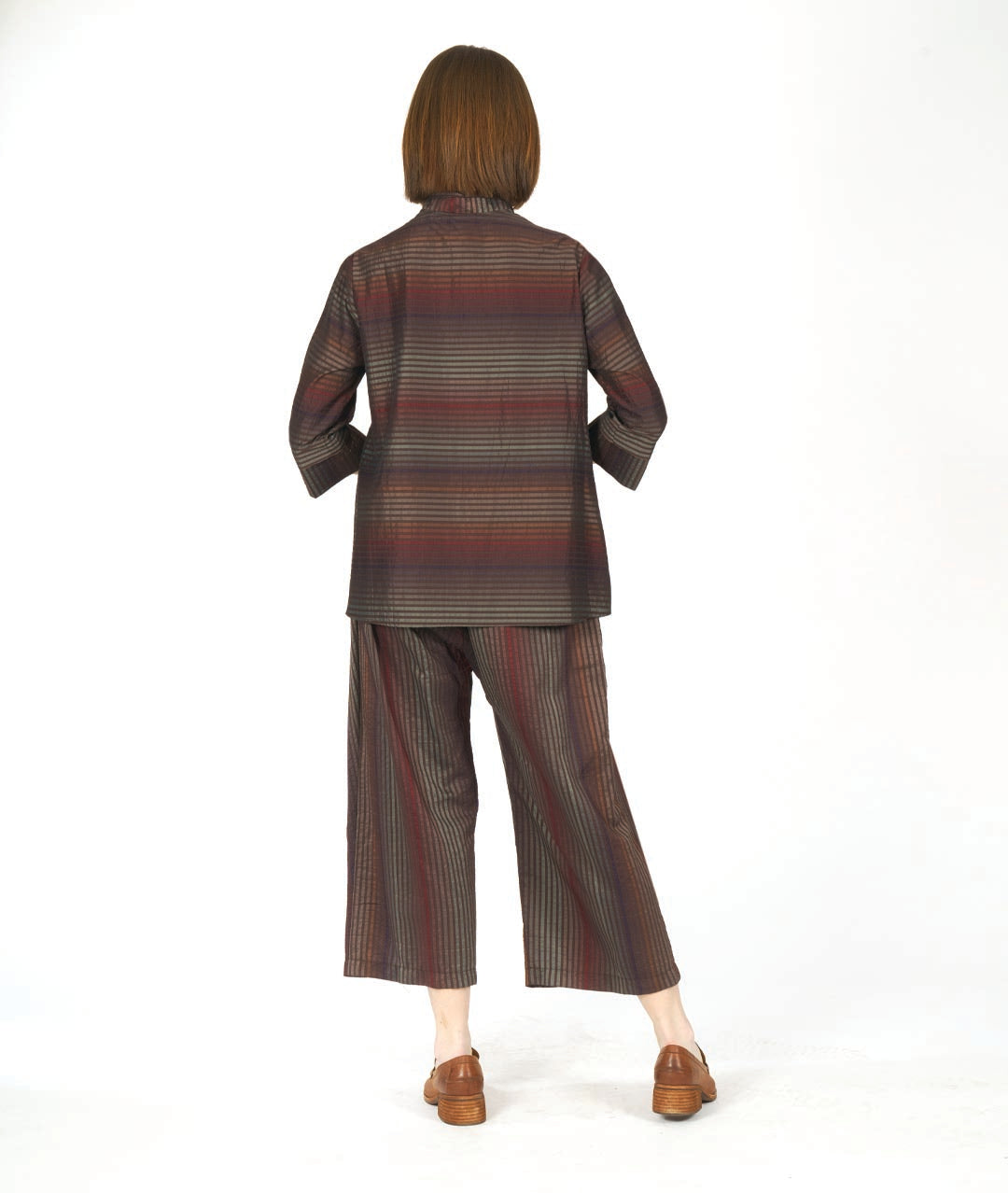 model in a red and brown tone striped pant with an overlap at each thigh. worn with a matching blouse with 3/4 sleeves with a wide cuff and a mandarin style collar