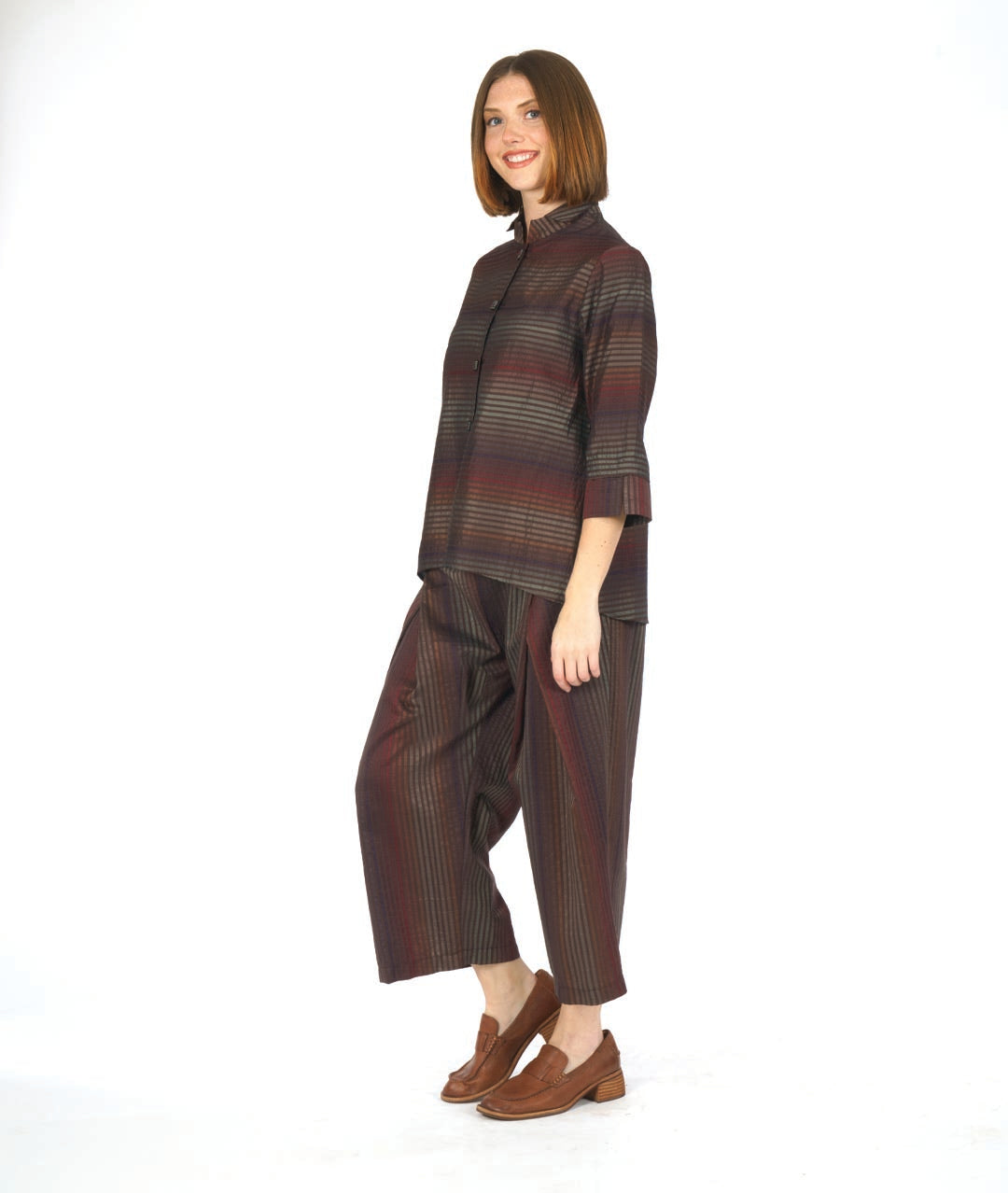 model in a red and brown tone striped pant with an overlap at each thigh. worn with a matching blouse with 3/4 sleeves with a wide cuff and a mandarin style collar