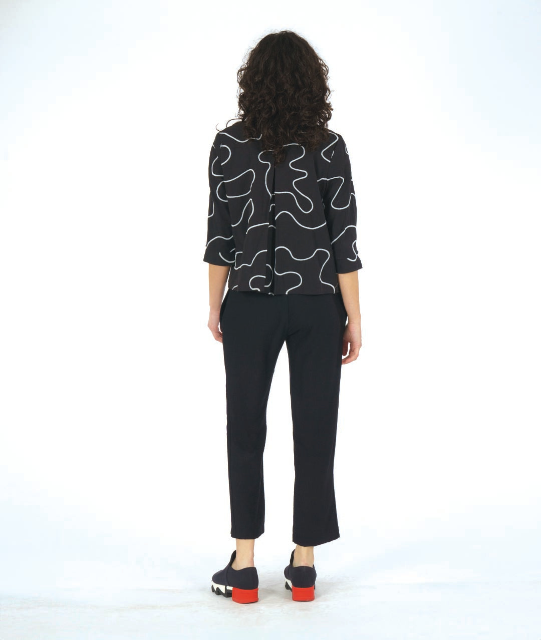 model in a black pant with a black button down with a white swirl embroidery and a twin button detail 