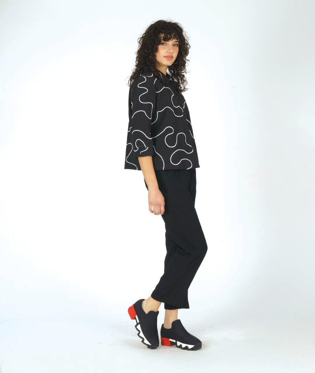model in a black pant with a black button down with a white swirl embroidery and a twin button detail 