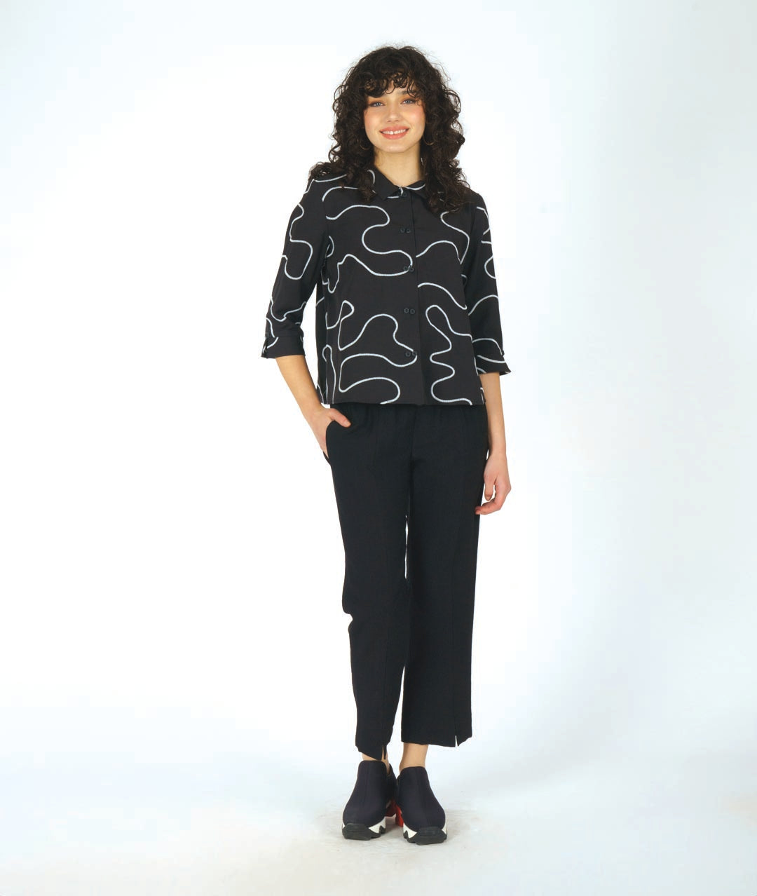 model in a black pant with a black button down with a white swirl embroidery and a twin button detail 