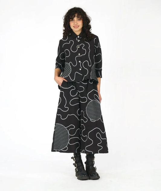 model wearing matching black and white swirl and circle patterned button-up top and wide leg pants against white background