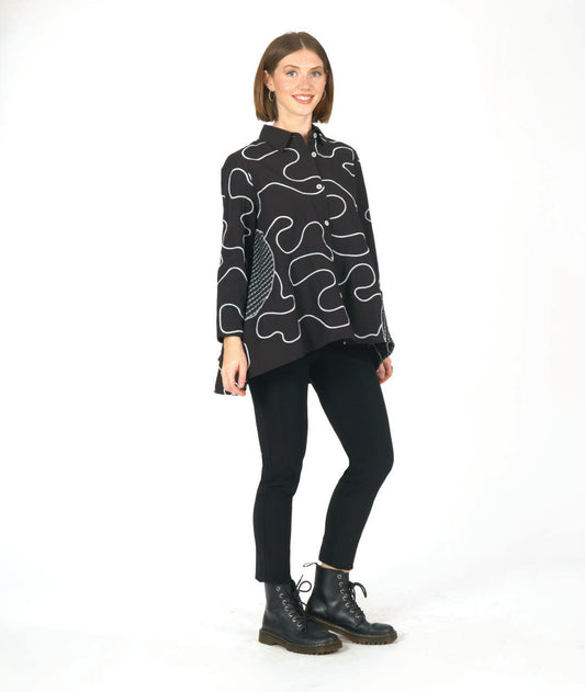 model in a black pant with a black button down blouse. blouse has a white swirl embroidery print and checkerboard patches