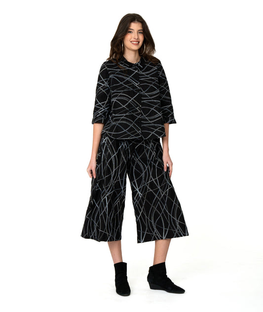 model in a wide leg black pant with a grey and blue embroidered stripe. worn with a matching button up blouse